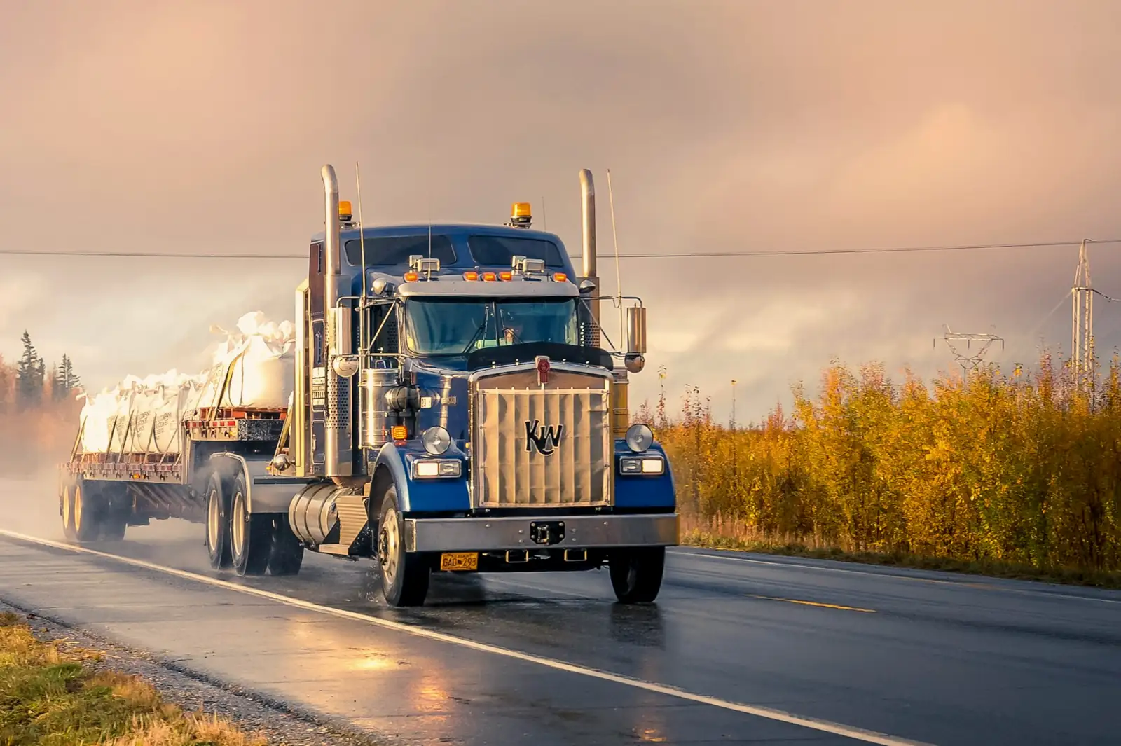 Kenworth semi-truck hauling a flatbed down a wet road at golden hour